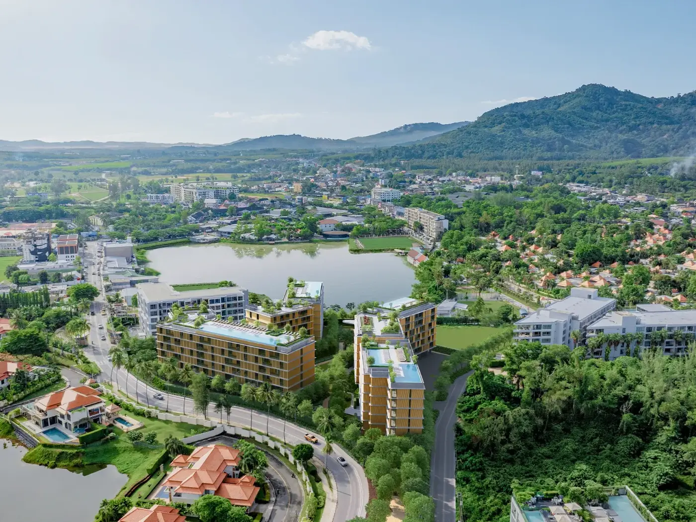 Aerial view of low-rise condominiums beside a lake with green hills behind